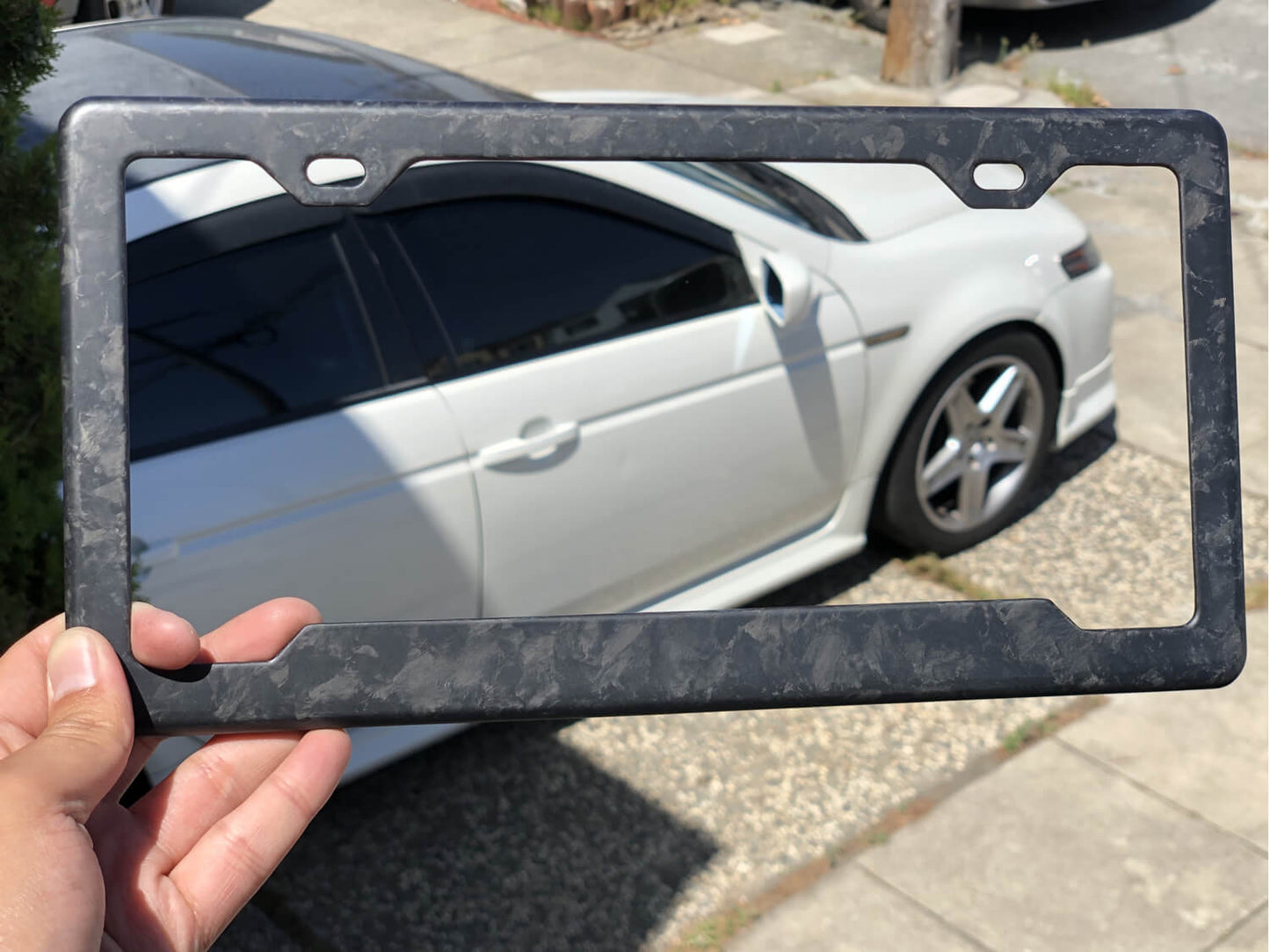 Forged Carbon Fiber License Plate Frame - 2 Holes Angled Bottom - Matte Finish being held by customer